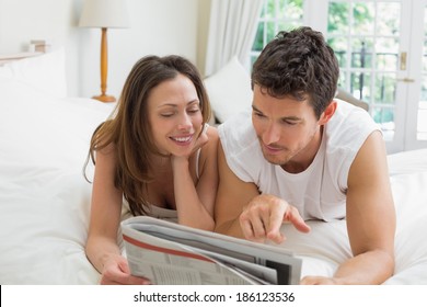 Relaxed Young Couple Reading Newspaper In Bed At Home