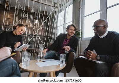 Relaxed Young Executives Having A Meeting Indoors. Multiracial Group Of People Sitting In Office Lobby Discussing Business.