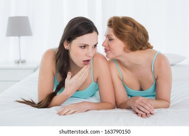 Relaxed young female friends in tank tops gossiping in bed at home