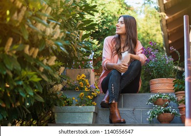 Relaxed young female smiling and looking side, sitting on home terrace. Hobby and resting leisure concept.