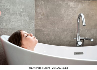 Relaxed young girl model wears towel wrapped on head, feels refreshed after taking shower, has healthy clean soft skin, poses in cozy bathroom. Girl, beauty and hygiene concept. High quality photo - Shutterstock ID 2312039613