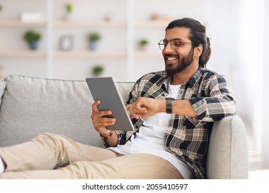 Relaxed Young Indian Man Chilling At Home With Digital Tablet, Sitting On Couch, Copy Space. Happy Guy Freelancer Shopping Online, Using Modern Pad And Smiling, Entertainment Concept