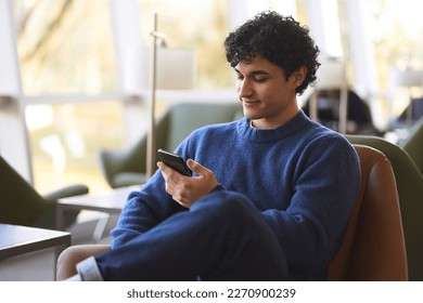 Relaxed young Latin American man using mobile phone, checking social media content, scrolling news feed, messaging, posting photos on his social account, ordering food, booking. People and technology - Powered by Shutterstock