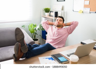 Relaxed young man because he finished all his work. Attractive guy with his feet up on his office desk, eyes closed and arms behind the head
