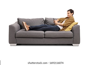 Relaxed young man lying on a sofa with a mobile phone isolated on white background