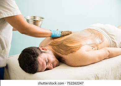 Relaxed Young Man Lying On A Massage Bed And Getting A Mud Bath In A Spa 