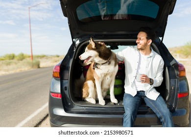 Relaxed young man petting his dog while smiling and resting in his car at the side of the road during a vacation trip - Shutterstock ID 2153980571