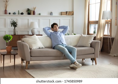 Relaxed Young Man Sit Rest On Couch In Modern Design Living Room Daydreaming Or Sleeping, Calm Millennial Male Relax On Sofa At Home, Breathe Fresh Air, Relieve Negative Emotion, Stress Free Concept