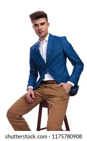 Relaxed Young Man Sitting On A Stool With One Hand In Pocket On White Background