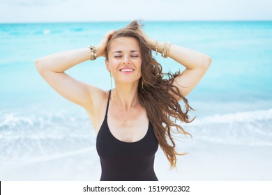 relaxed young middle age woman with long curly hair in elegant black bathing suit on a white beach having fun time.
