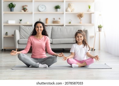 Relaxed young mother and little daughter in sportswear sitting on fitness mat in lotus position and smiling, meditating together at home, copy space. Healthy family, sports lifestyle concept - Powered by Shutterstock