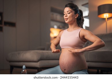 A relaxed young pregnant woman exhaling while doing breathing exercises and meditating at home. - Powered by Shutterstock