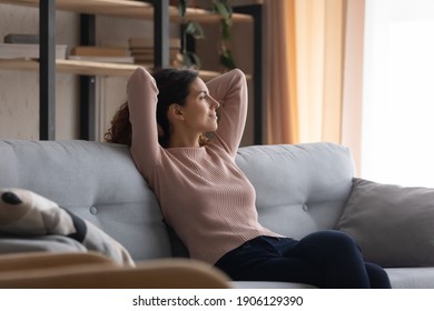 Relaxed Young Smiling Pretty Woman Sitting On Cozy Couch, Looking In Distance, Dreaming Or Visualizing Future, Recollecting Memories, Enjoying Stress Free Peaceful Weekend Holiday Time At Home.