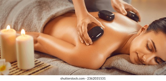 Relaxed young woman enjoying body treatment at wellness center. Beautiful serene girl lying on couch getting hot stone massage in spa salon. Beauty treatment therapy, body care concept - Powered by Shutterstock