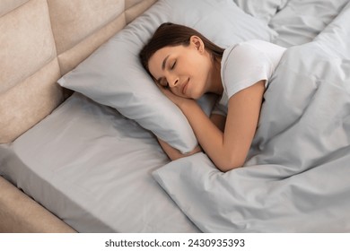 Relaxed young woman enjoying serene sleep, curled up in cozy bed with soft pillows and tranquil expression, illustrating peaceful rest, above view - Powered by Shutterstock