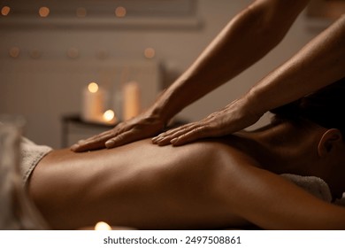 Relaxed young woman lying face down enjoying professional back massage in serene spa setting with candles, side view - Powered by Shutterstock