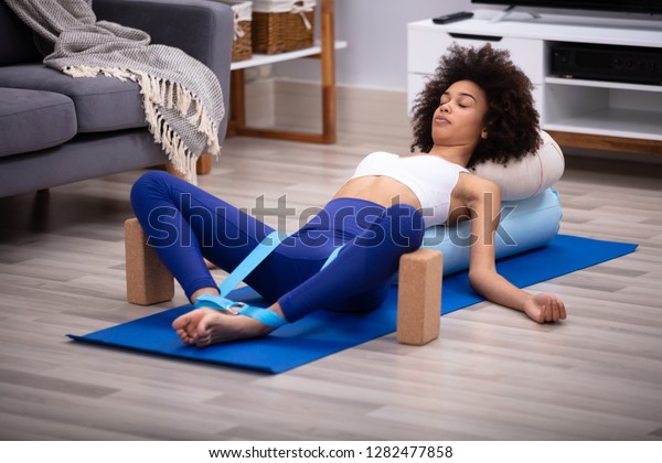 Relaxed Young Woman Lying On Fitness Mat Doing\
Exercise With Yoga Belt And Two\
Blocks