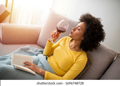 Relaxed young woman reading a book. Woman At Home Lying On Reading Book And Drinking Wine. Beautiful young African woman enjoying a glass of wine - Powered by Shutterstock