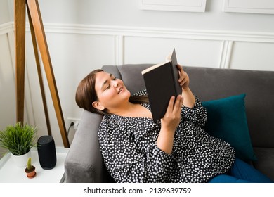 Relaxed Young Woman Reading A Book While Resting In The Couch. Happy Obese Woman Enjoying A Novel