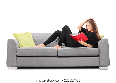 Relaxed Young Woman Reading A Book Seated On Sofa Isolated On White Background