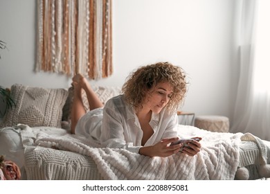 Relaxed young woman watching movie on smartphone lying on bed - Shutterstock ID 2208895081