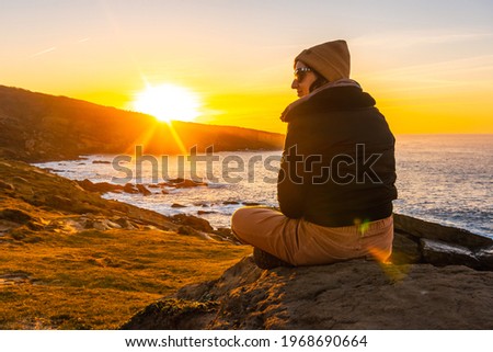 A relaxed young woman watching the sunset in the cove of stones in the Jaizkibel mountain in the town of Pasajes, Gipuzkoa. Basque Country