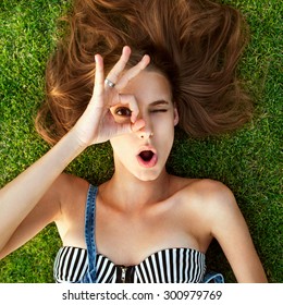 Relaxing after long trip. Top view of beautiful young woman  lying on the grass, hands shows gesture ok