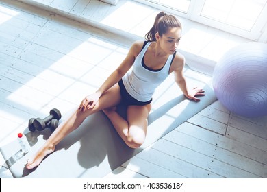 Relaxing after training. Top view of beautiful young woman looking away while sitting on exercise mat at gym - Powered by Shutterstock