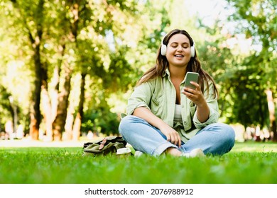 Relaxing caucasian young freelancer teenager student woman listening to the music song singer playlist radio podcast sitting in lotus position in musical mobile application in park