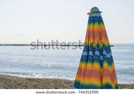 Colorful striped, closed parasol in close-up on the beach at sunset