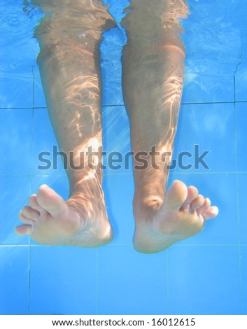 Relaxing day; underwater picture of legs on the swimming pool.