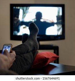 relaxing feet of man watching a movie and looking to cell phone