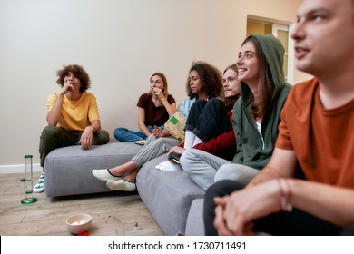 Relaxing With Friends. Young Multicultural People Having Fun, Eating Snacks And Talking, Sitting On The Coach At Home. Smoking Marijuana From A Bong. Home Party. Cannabis Weed Legalization, Ganja