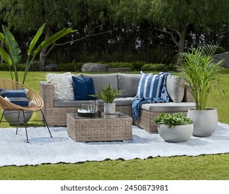 Relaxing garden lounge set against a lush landscape, with a rattan sectional sofa adorned with cozy cushions, complemented by a unique acapulco chair, and concrete planters adding a touch of greenery. - Powered by Shutterstock