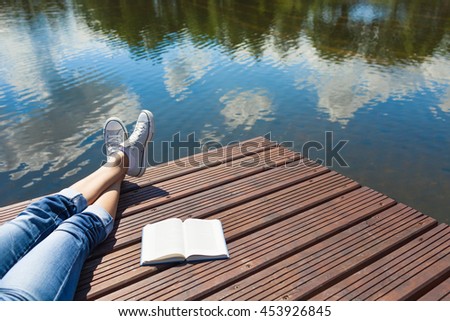 Relaxing holiday by the lake. Woman's feet relaxing on a wooden dock with book at her side. 