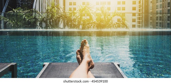Relaxing in holidays, Panoramic asian guy feet on sun bathing bed at swimming pool in the city