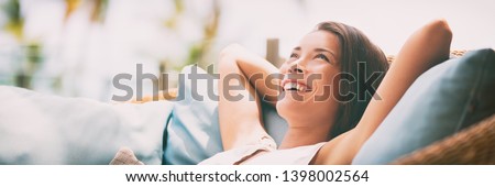 Relaxing home lifestyle happy woman in relax luxury hotel room sofa lying back with arms behind head smiling. Asian girl in comfortable lounging chair travel living.