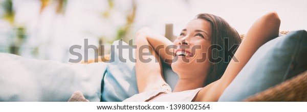 Relaxing home lifestyle\
happy woman in relax luxury hotel room sofa lying back with arms\
behind head smiling. Asian girl in comfortable lounging chair\
travel living.