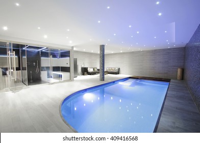 Relaxing indoor swimming pool with lighting and a corner for rest. Luxury resort swimming pool with beautiful clean blue water and  light effects around the swimming pool. 
