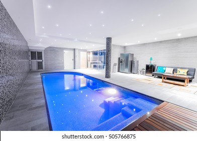 Relaxing indoor swimming pool with lighting and a corner for rest. Luxury resort swimming pool with beautiful clean blue water and light effects around the swimming pool.