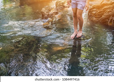 Relaxing for life, natural therapy concept : Young man's feet walkiing on rocks with clear, cold water. Feel comfortable and relax in nature of forest with water flowing  on summer day