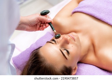 Relaxing massage. Side view european woman getting massage with jade face roller gouache in spa salon