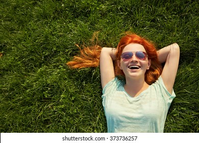 relaxing redhead girl lying on the grass. woman in sunglasses relaxation outdoor