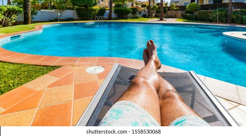 Relaxing at the swimming pool. Man relaxing next to swimming pool. Man enjoying the hot summer at swimming-pool. Sunbathing by the swimming pool, mans legs lying down on a sun lounger over the water. - Powered by Shutterstock