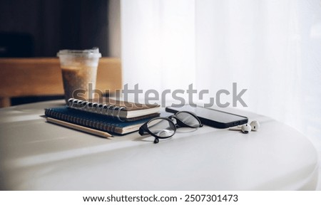 Relaxing time after work in cafe, eyeglasses with mobile, ear phone and notebook for writing diary during a day placed on white table by the window, Vintage color tone