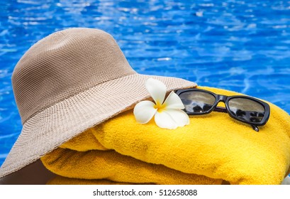 Relaxing times Concept: Hat,Yellow towel,sunglasses beside the pool with a beautiful Frangipani flower