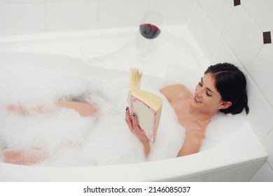 Relaxing In The Tub. Cropped Shot Of A Young Woman Relaxing In The Bathtub With A Book And Glass Of Wine.