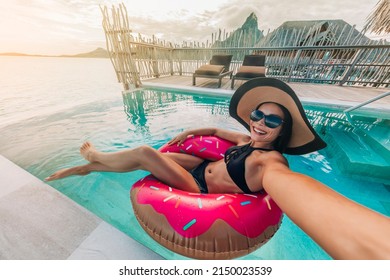 Relaxing woman floating in donut inflatable swimming pool toy at luxury resort taking selfie photo using sunbathing. Travel vacation hotel lifestyle - Powered by Shutterstock