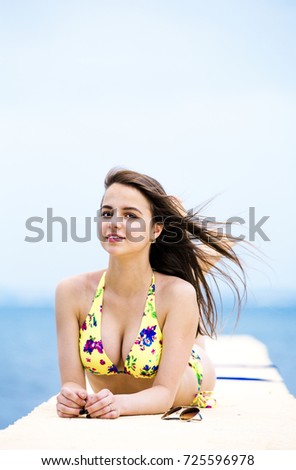 Relaxing young woman on pier at the sea in summer day. Skinny girl in swimsuits posing near sea. 