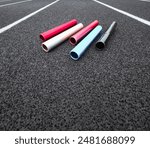 Relay Batons on a Running Track. Multi-colored aluminum relay batons rest on a black running track with white lane lines. Texturized artificial black surface.